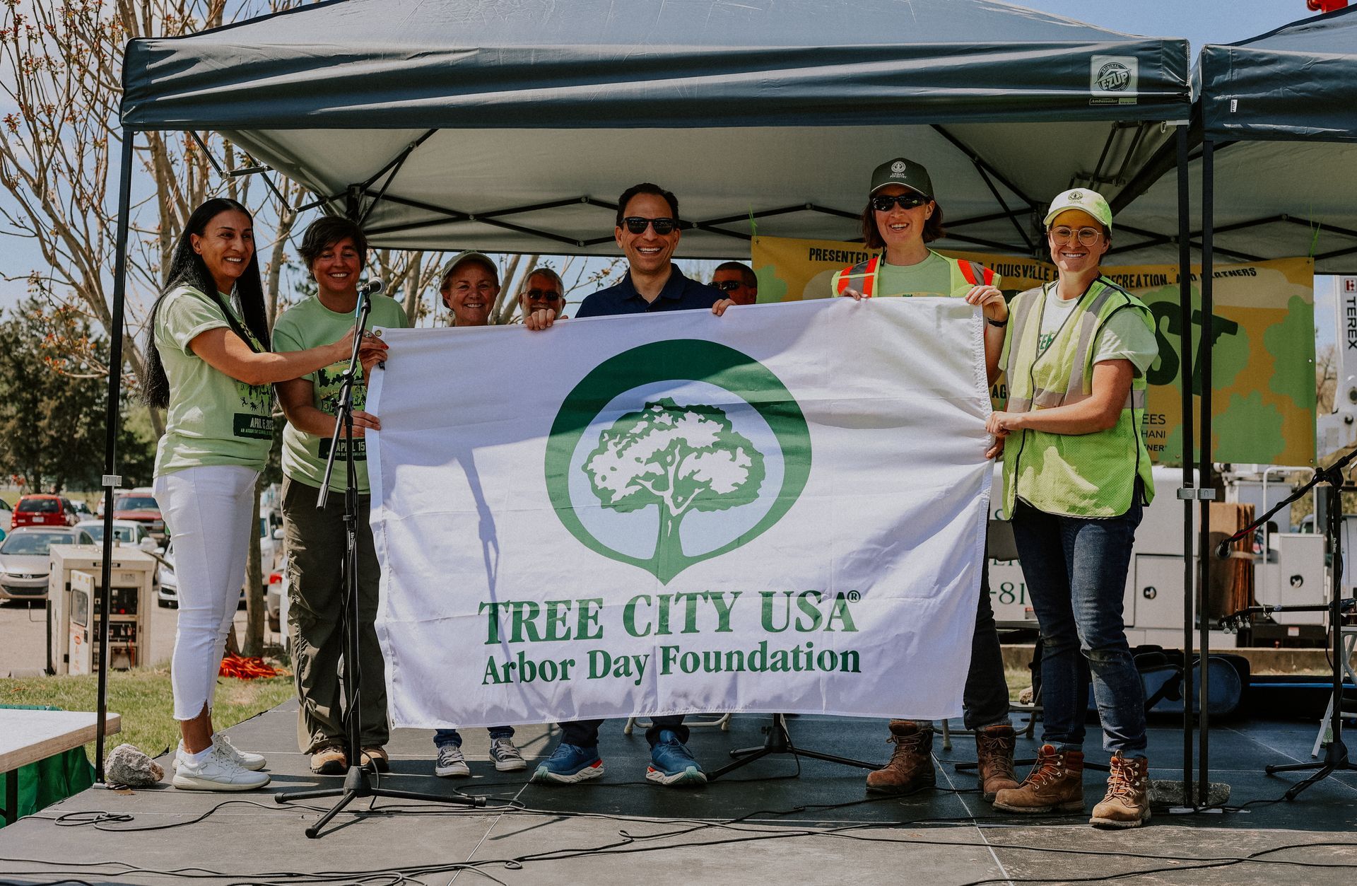 City and nonprofit officials posing with Mayor Craig Greenberg with Tree City USA flag at TreeFest 2023