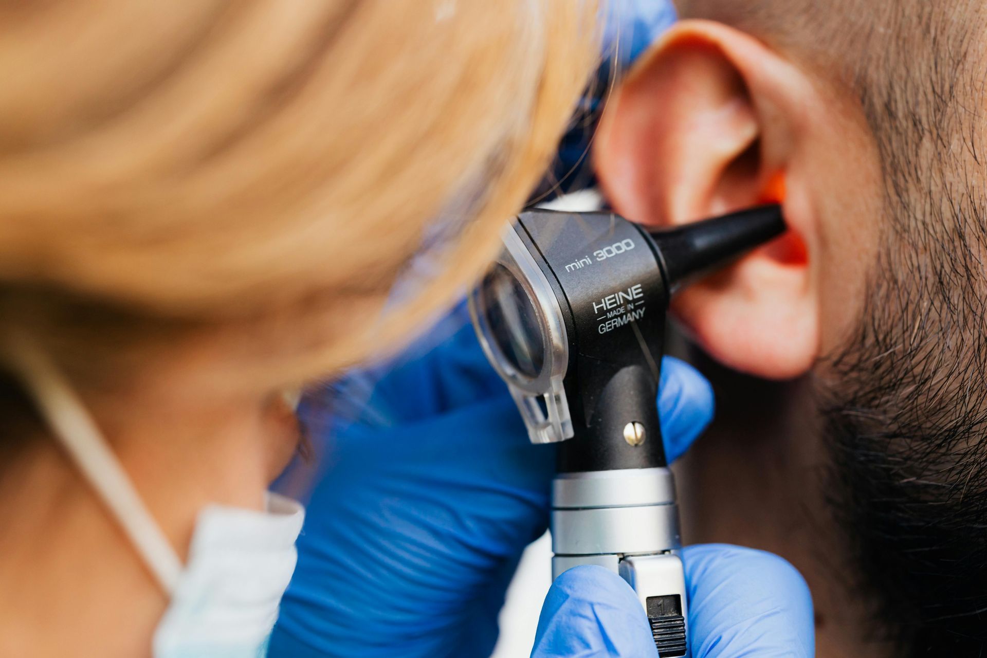 A medical professional wearing blue gloves uses an otoscope to examine a person's ear.