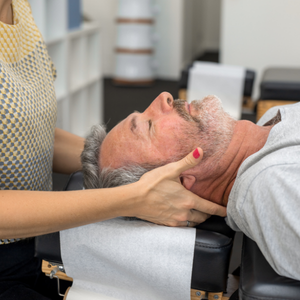 A practitioner performs a neck adjustment on a person lying on their back on a clinical table.