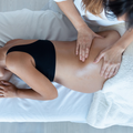 A massage therapist performs a massage on a person's back, who is lying on a treatment table covered with a white sheet.