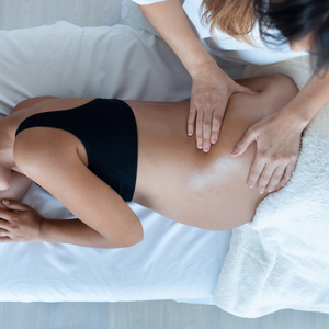 A massage therapist performs a massage on a person's back, who is lying on a treatment table covered with a white sheet.