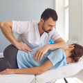A chiropractor performs a spinal adjustment on a patient lying on a treatment table in a clinic.