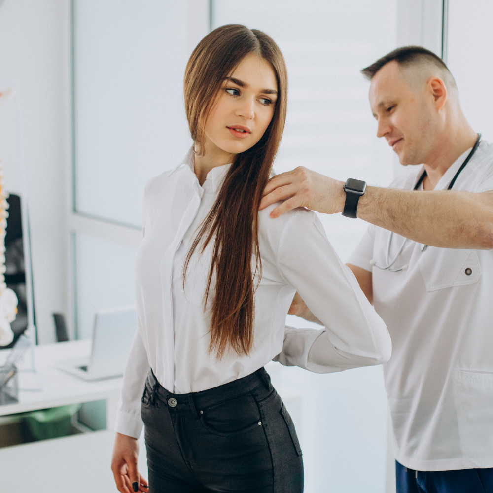 A doctor examining a patient's back in a brightly lit medical office.