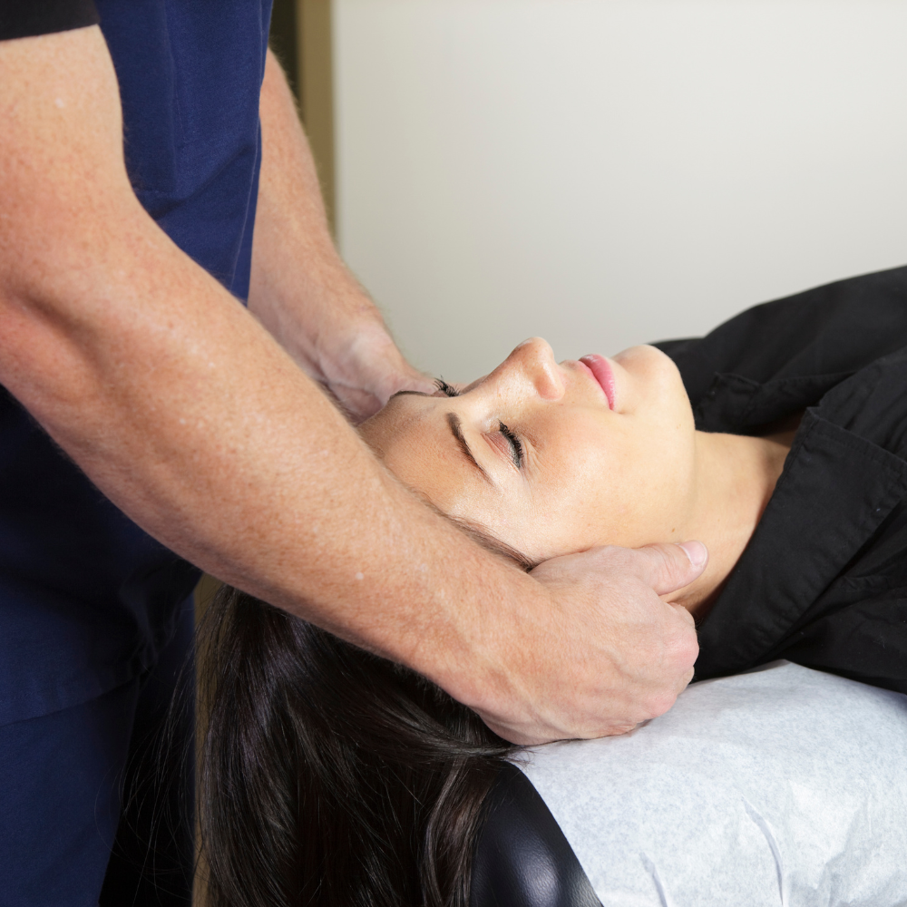A healthcare practitioner performs a manual adjustment on a person's neck while they lie on an exam table.