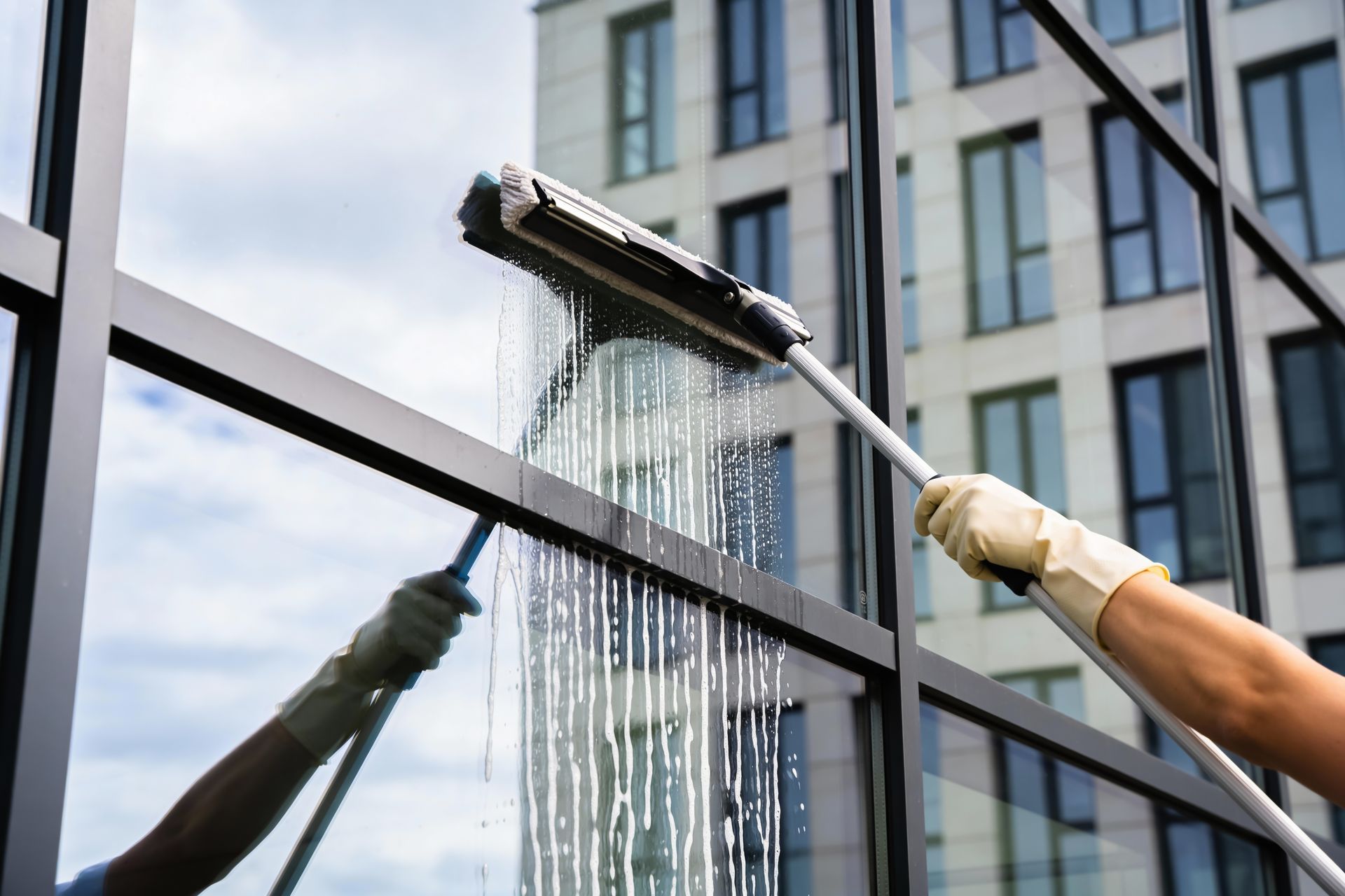 Window cleaner washing a glass building exterior with a squeegee