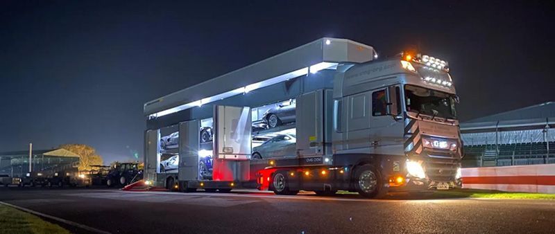 A large, illuminated car transporter truck at night; showcasing vehicles on multiple levels.