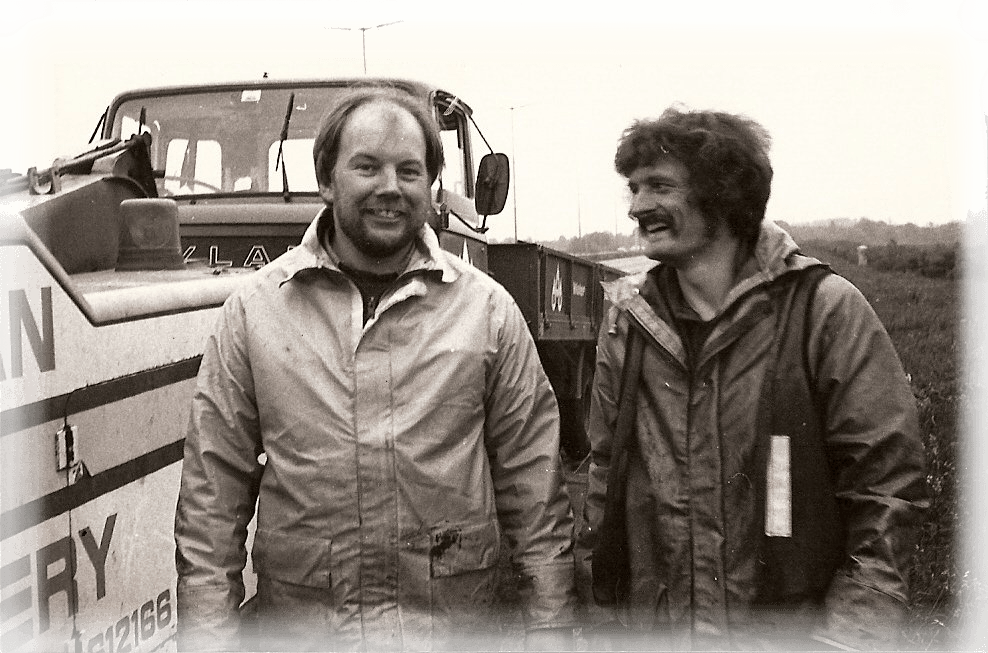 two men standing in front of a truck that says machinery