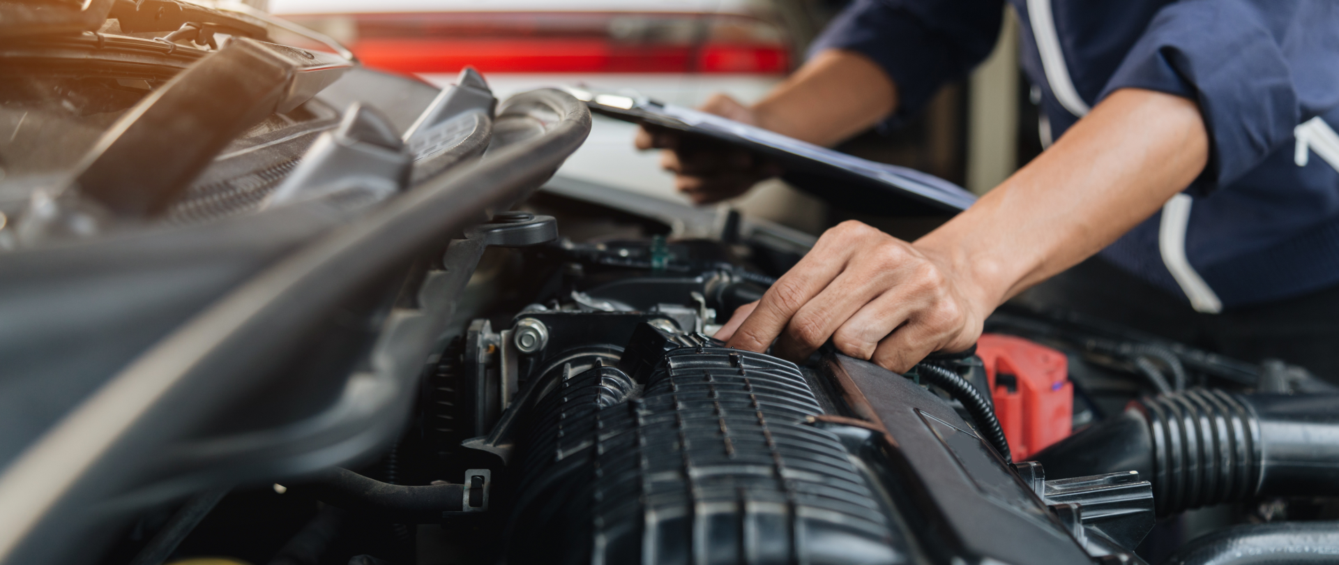 A man is working on the engine of a car while holding a clipboard.