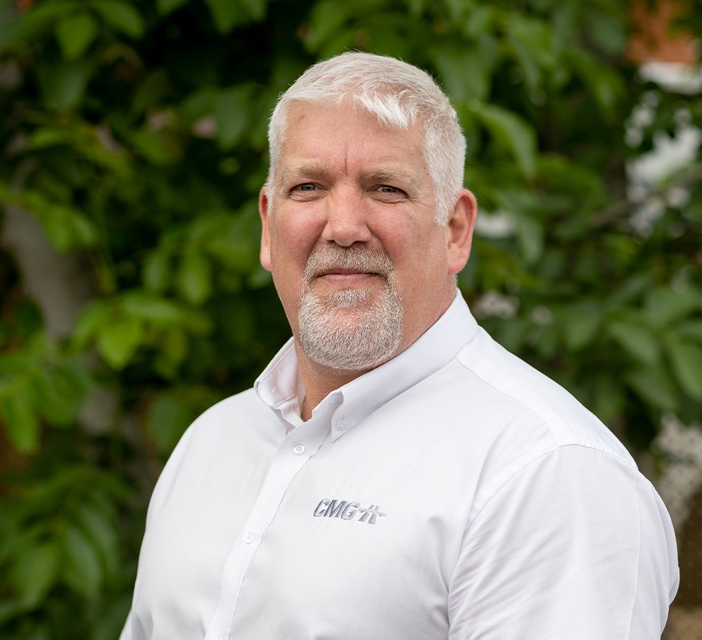 A man with a beard is wearing a white shirt and standing in front of a tree.