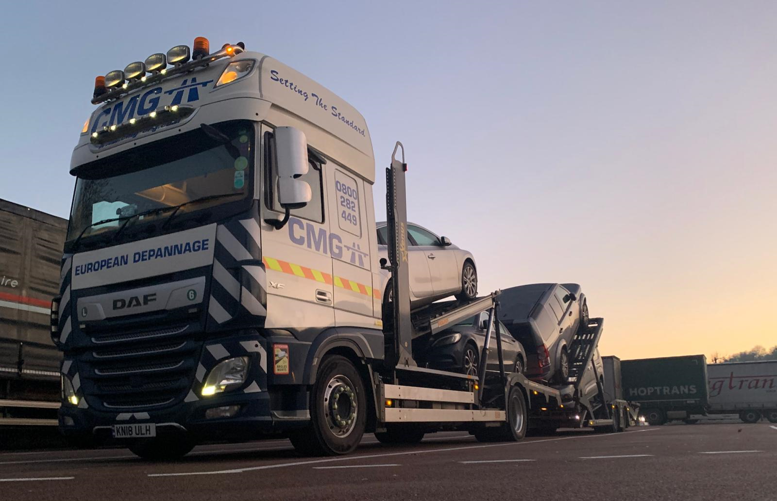 A large truck is carrying two cars on a trailer.