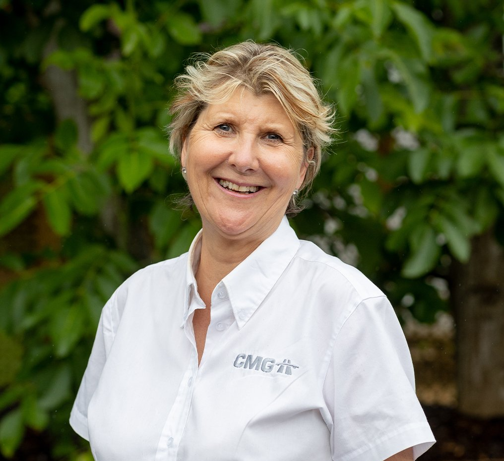 A woman in a white shirt is smiling in front of a tree.