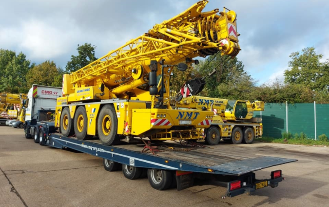 a large yellow nmt crane is on a flatbed trailer
