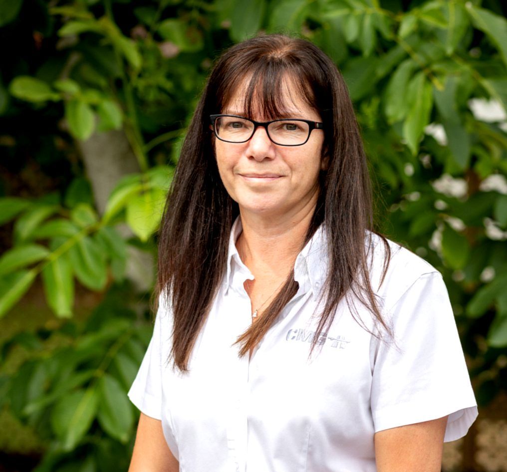 A woman wearing glasses and a white shirt is standing in front of a tree.