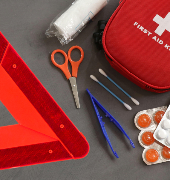 Emergency supplies: red warning triangle, first aid kit, bandages, scissors, pills, tweezers, and cotton swabs.
