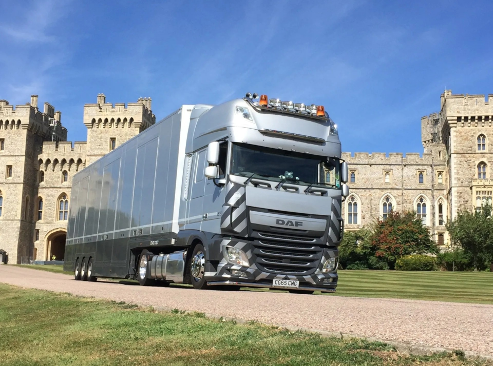 A large truck is driving down a gravel road in front of a castle.