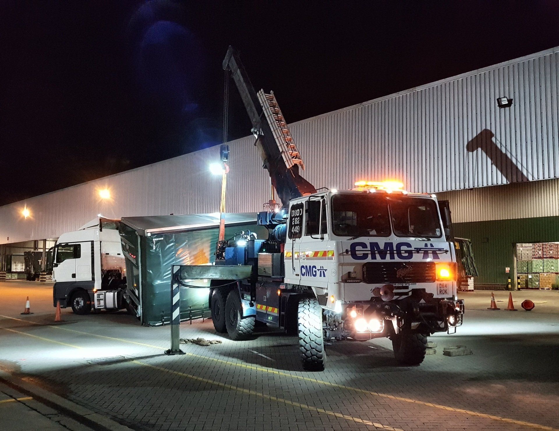 a truck with a crane attached to it is parked in front of a building at night .