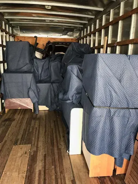 Moving truck interior loaded with furniture covered in blue quilted pads.