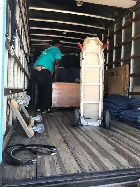Man in blue overalls lifting a tan couch against a white wall. Man in blue overalls lifting a tan couch against a white wall.