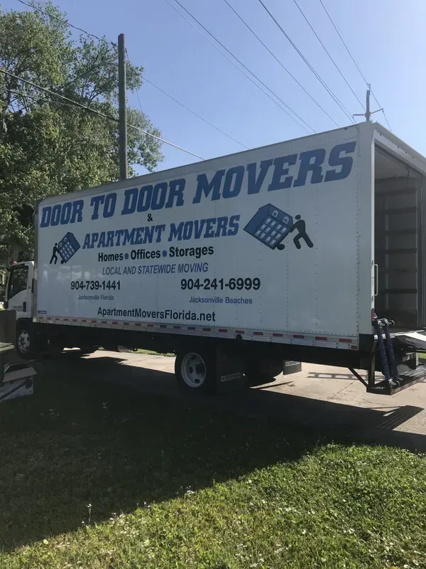 White moving truck with open back door, Door to Door Movers logo, sunny day.