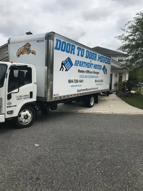 Moving truck parked in front of a house; Door to Door Movers logo on the side.