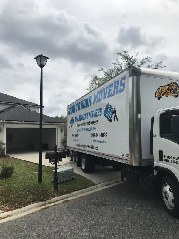 Moving truck parked in front of a house. Best Florida Movers logo on the truck. Cloudy sky.