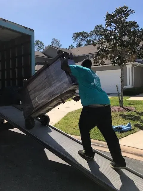 Man pushing furniture up a ramp into a truck on a sunny day.