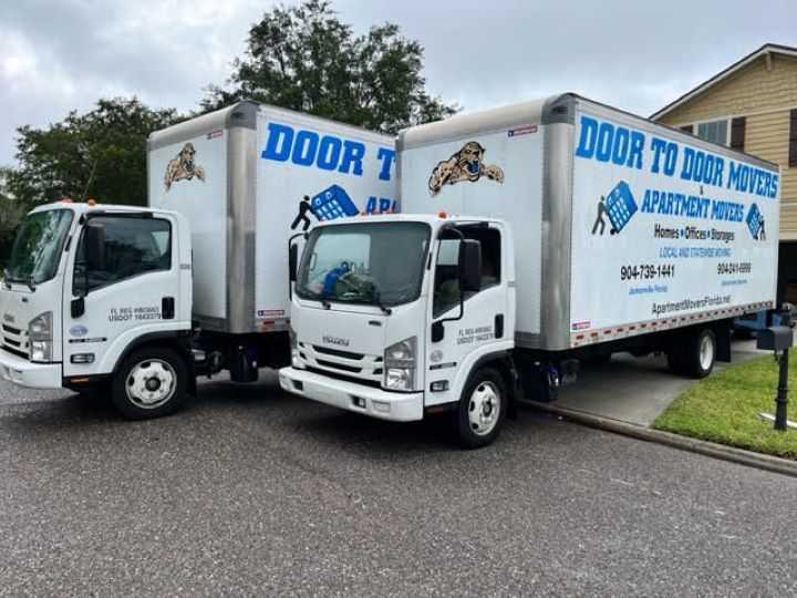 Two white moving trucks parked on a residential street; the trucks have Door to Door Movers logos.
