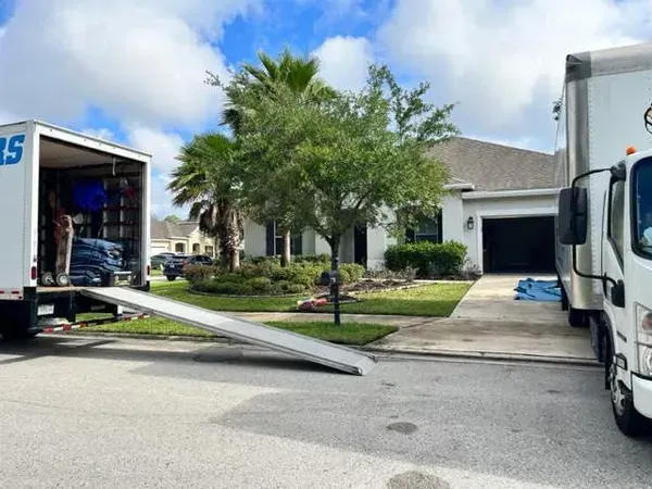 Moving trucks parked in front of a house. One truck has ramp down.