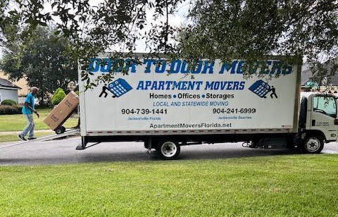 Moving truck with Door to Door Movers logo, on grass, with person carrying a box. Moving truck with Door to Door Movers logo, on grass, with person carrying a box.