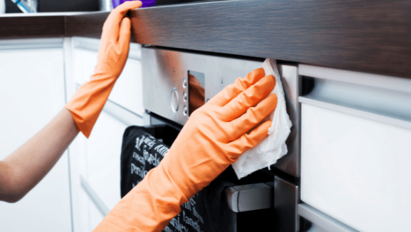 Oven Cleaning Bexhill. A cleaning operative wipes clean an oven with visible orange rubber gloves.
