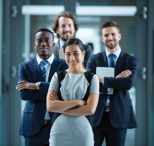 Business team, arms crossed, smiling in hallway, wearing suits.