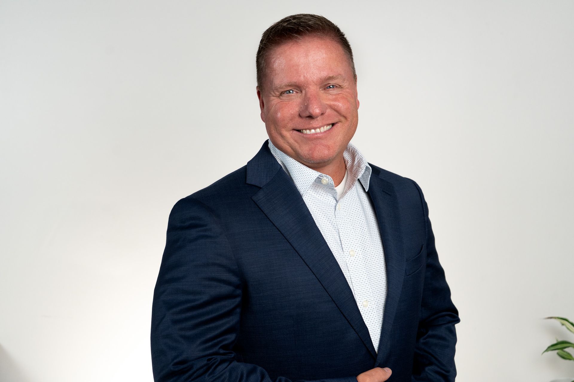 Man in blue blazer smiles, posing against a light gray background.