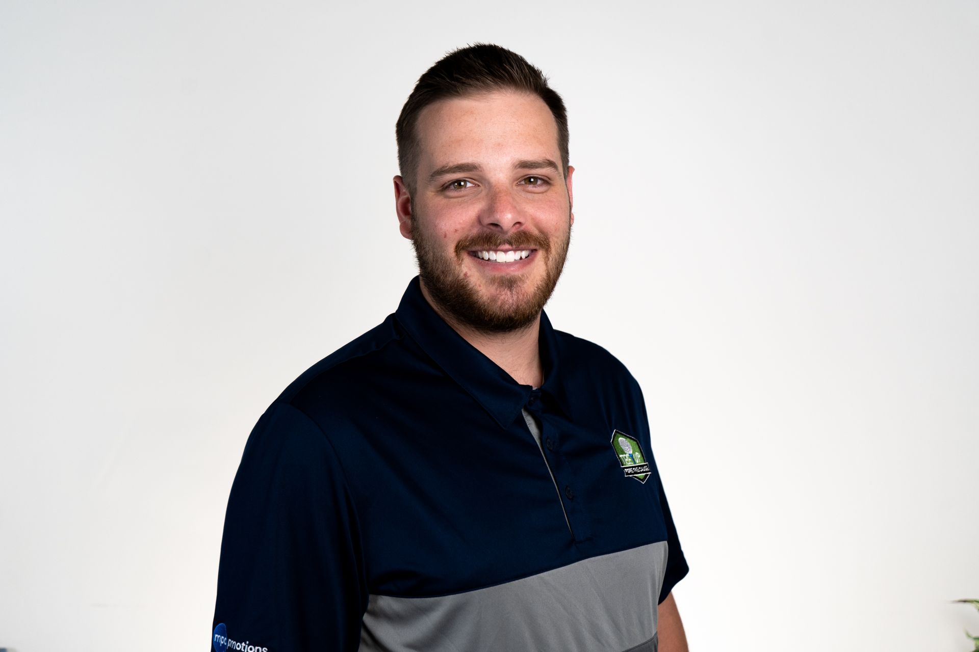 Man with a beard smiles under a wooden pier at the beach, wearing a striped shirt.