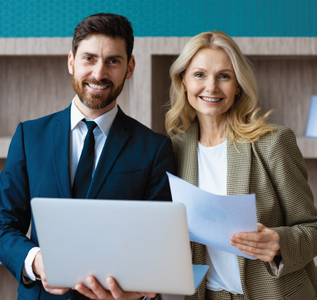 Man holding laptop and woman holding papers, both smiling, in an office setting.