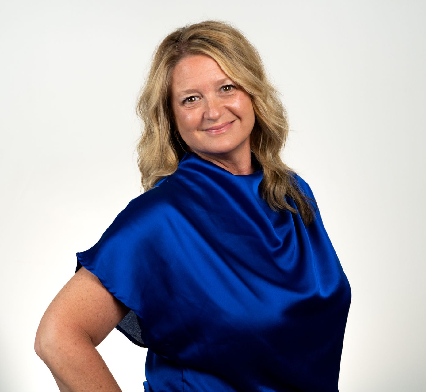 Woman with blonde hair in a bun wearing tortoise-shell glasses, smiling, resting on a floral cushion.