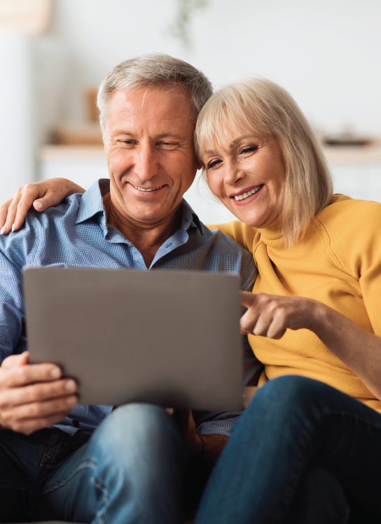 Smiling couple sitting close, looking at a laptop together; woman points at the screen.