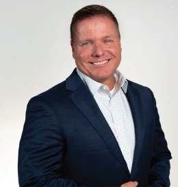 Man in blue blazer smiles, posing against a light gray background.