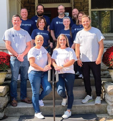 Group of people in matching shirts posing on steps of a building.
