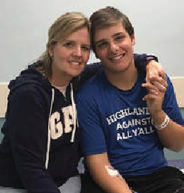 Woman and young person smiling, indoors. Young person in blue shirt with IV in arm.