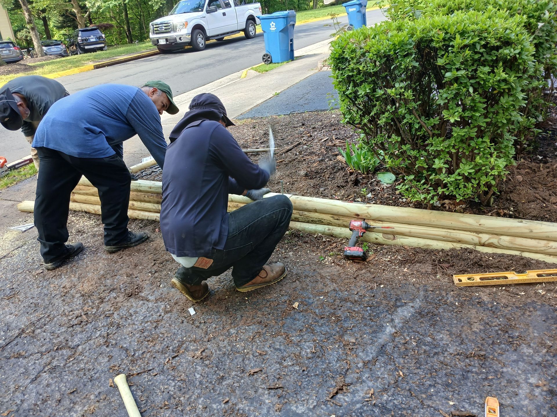 Two men are working on a wooden fence in the dirt.