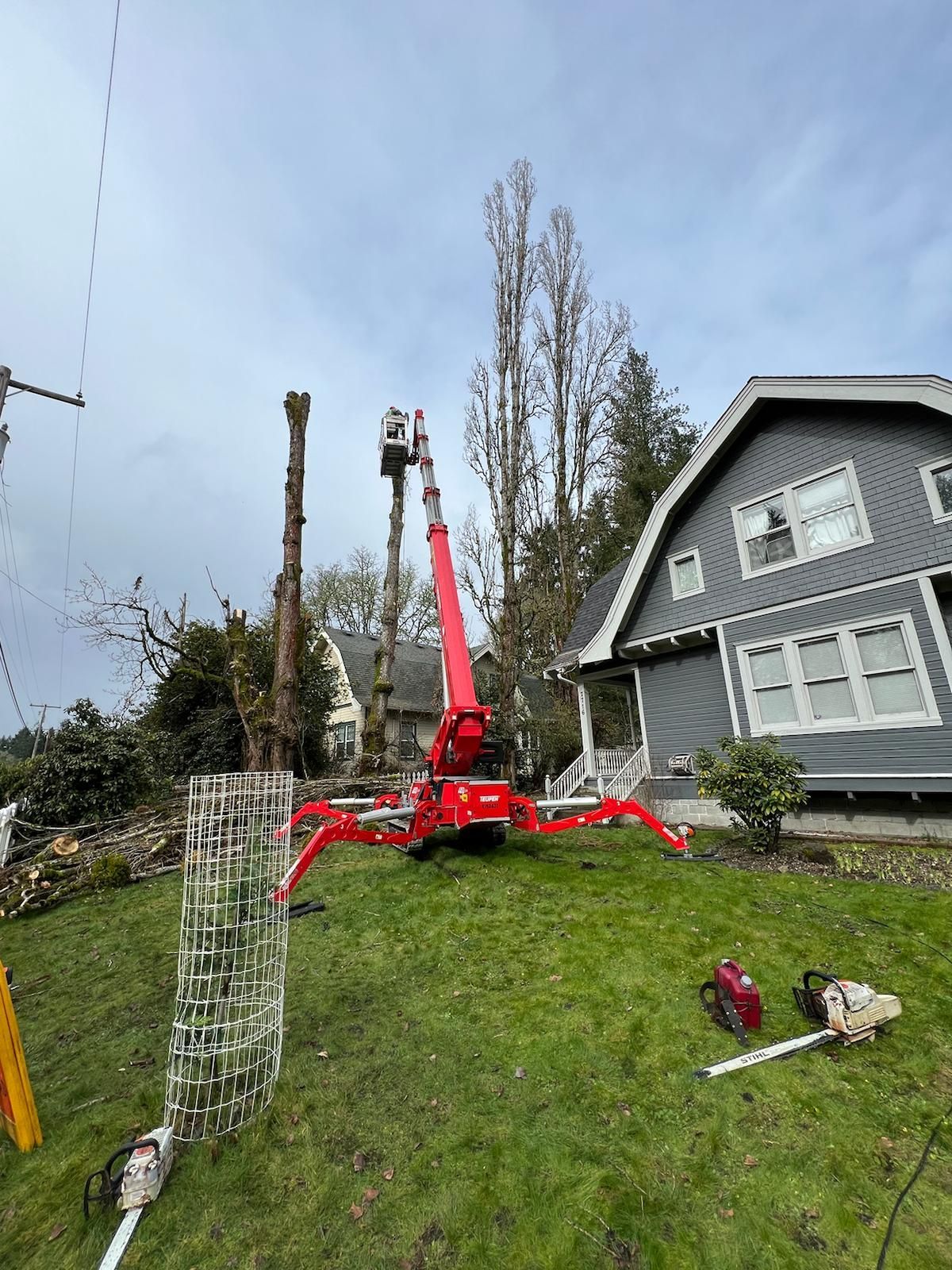 A red crane is cutting a tree in front of a house.