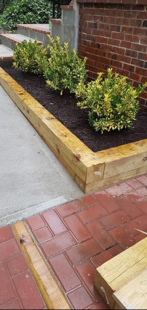 A wooden planter with plants in it next to a brick wall.