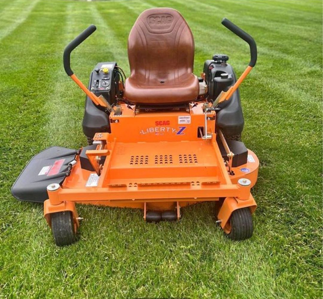 An orange lawn mower with a brown seat is parked in the grass