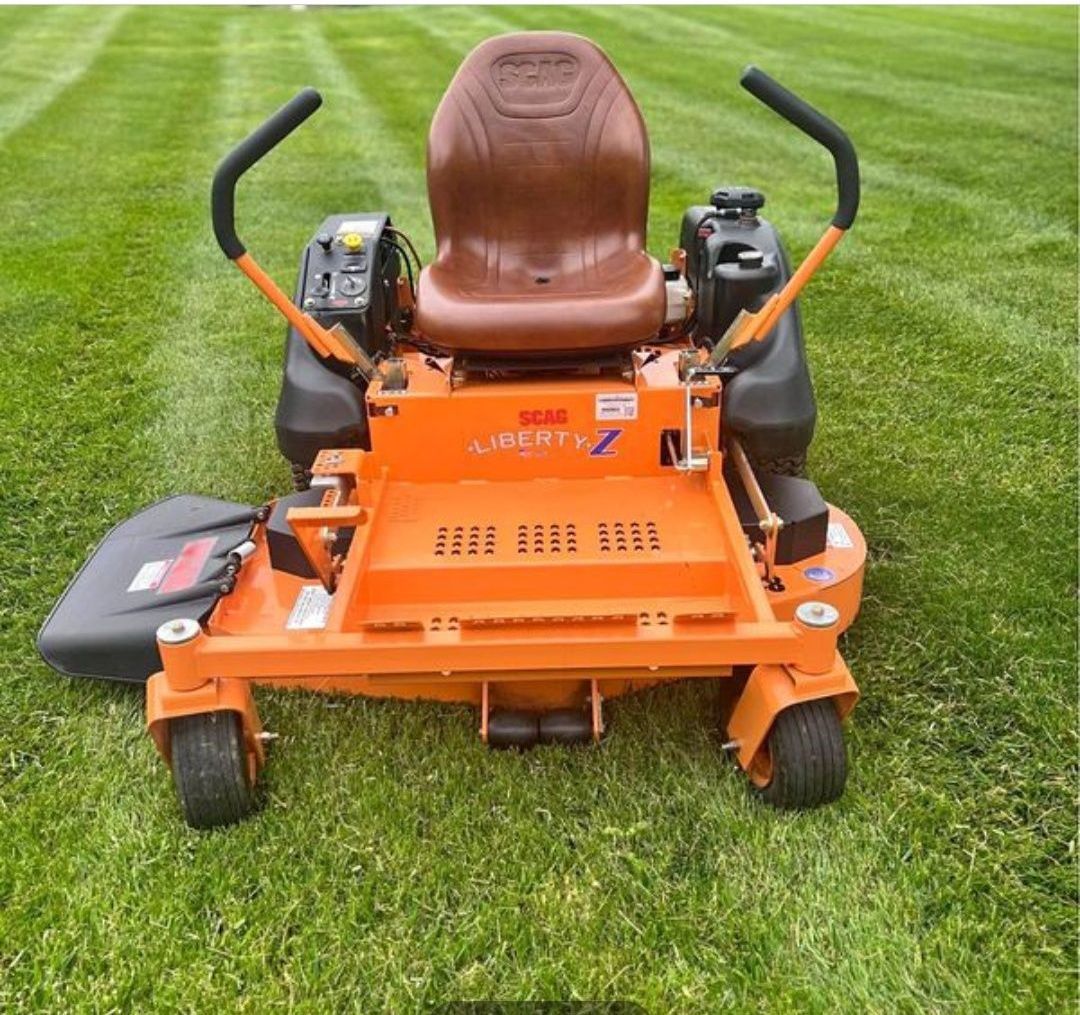An orange lawn mower with a brown seat is sitting in the grass