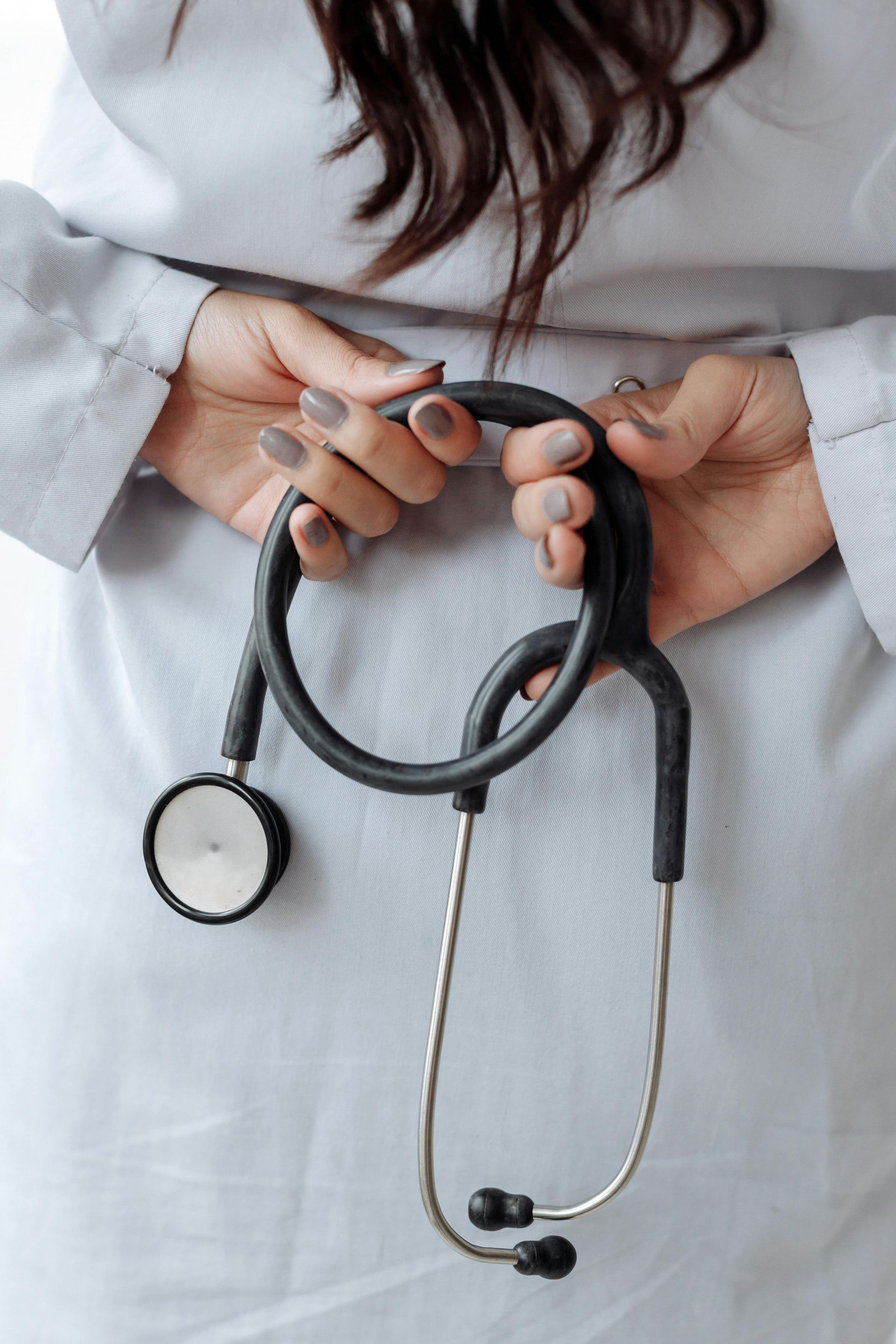 A woman in a white coat is holding a stethoscope in her hands.