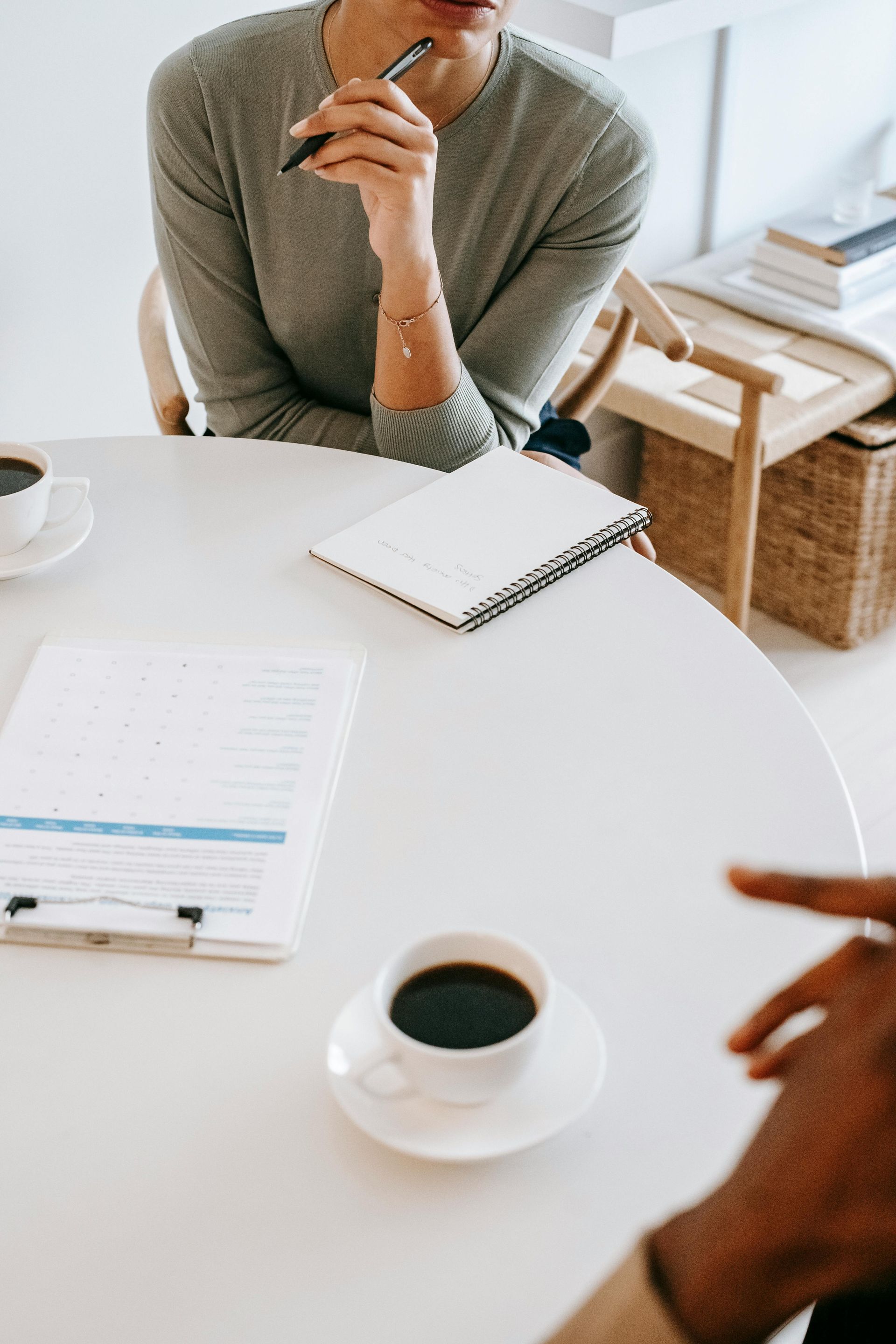 A woman is sitting at a table with a cup of coffee and a notebook.