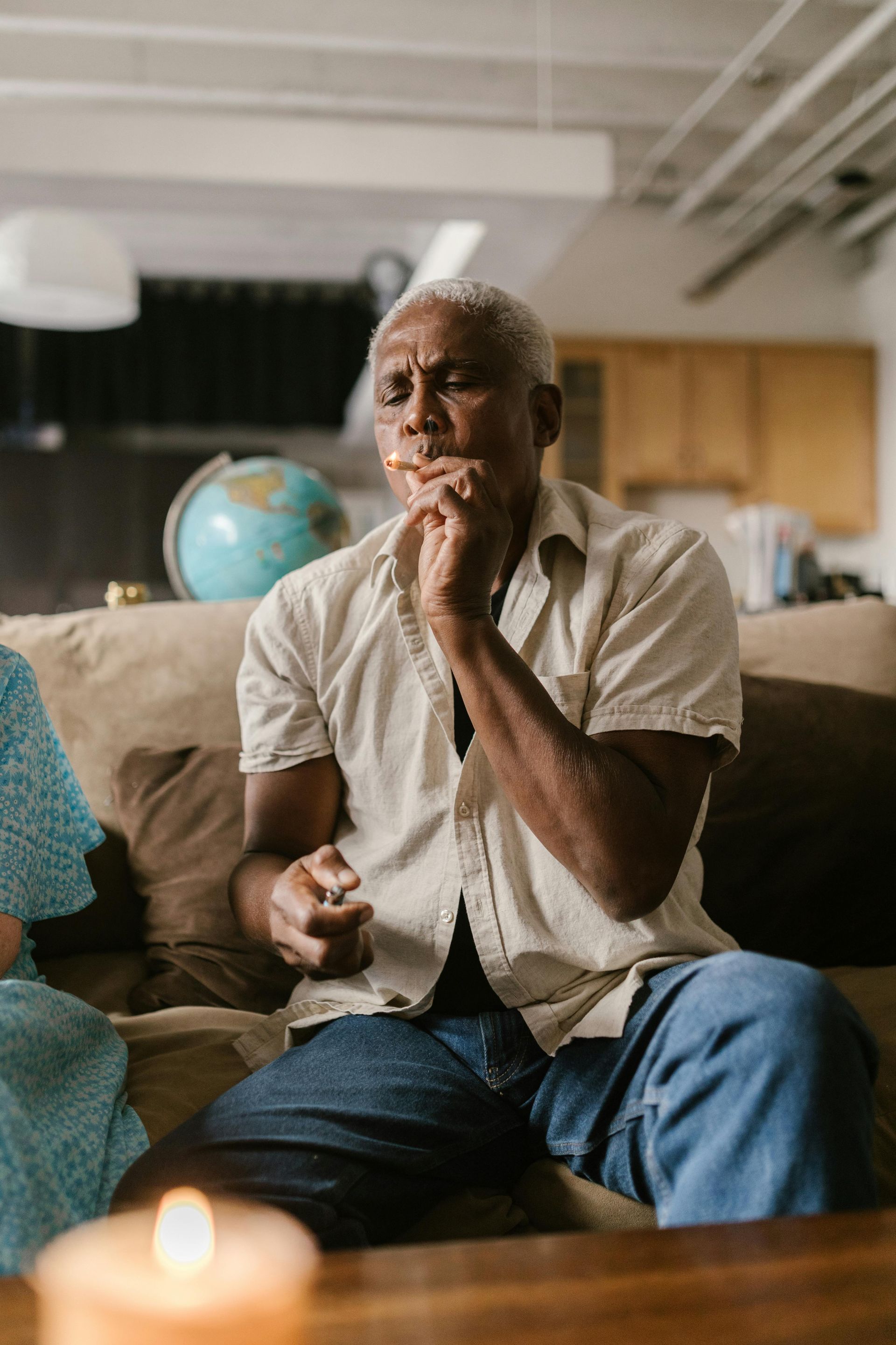 An elderly man is sitting on a couch with a candle in front of him.