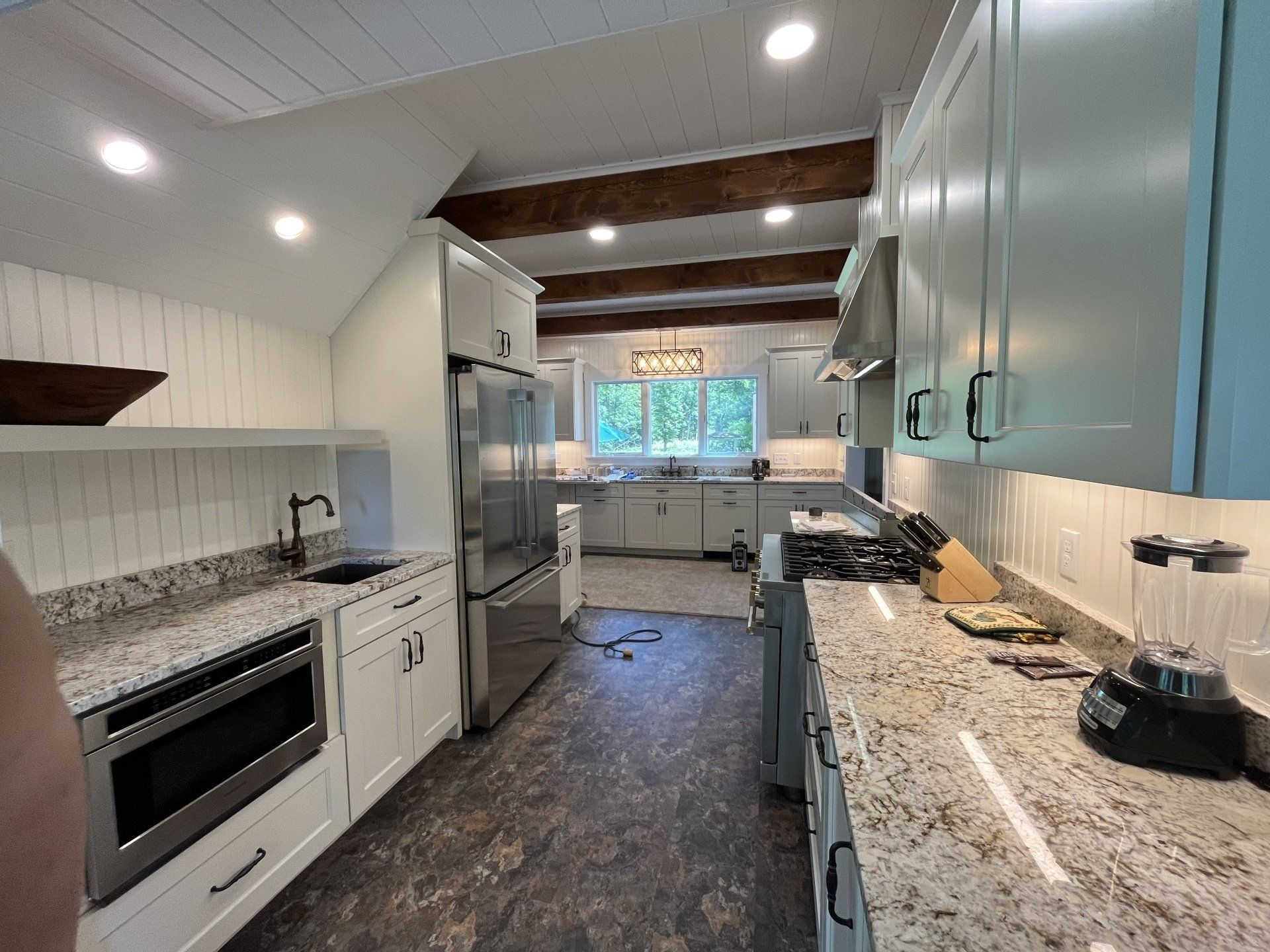 Kitchen with white cabinets, granite countertops, stainless steel appliances, and wood beams.