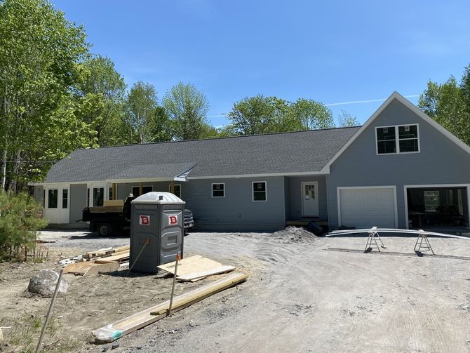 New construction home with light gray siding and gray roof, in a gravel driveway.