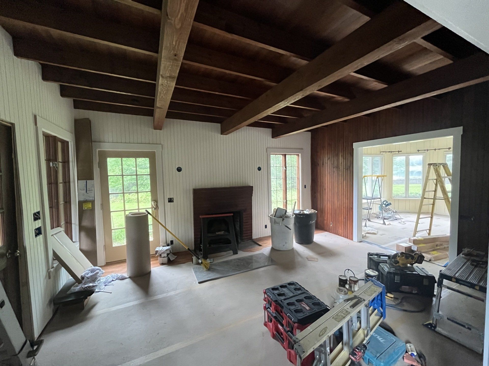 Interior room under renovation with dark wood beams, fireplace, and open doorway.